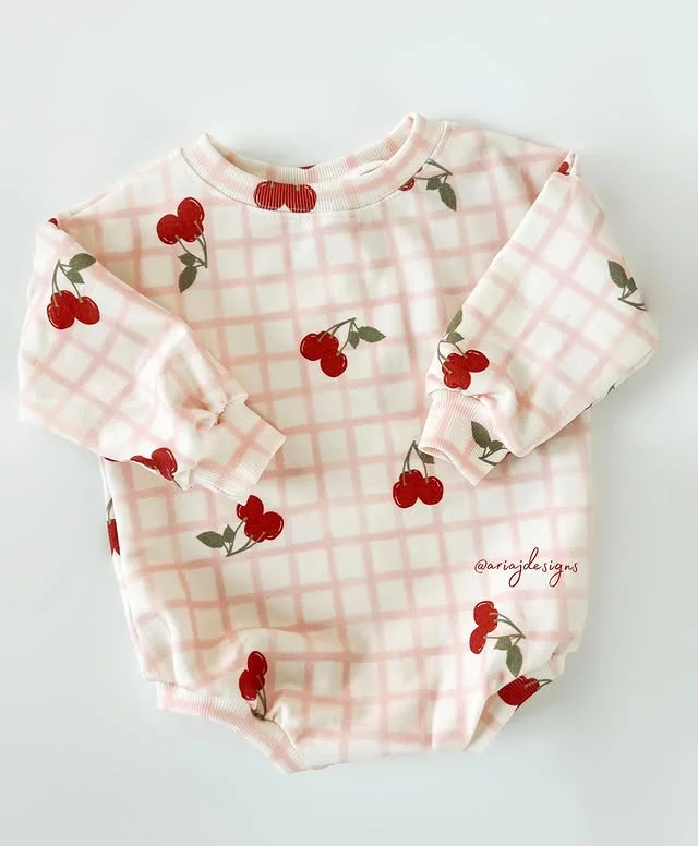 A sweater romper made with organic cs french terry fabric that features a pink plaid design with red cherries.