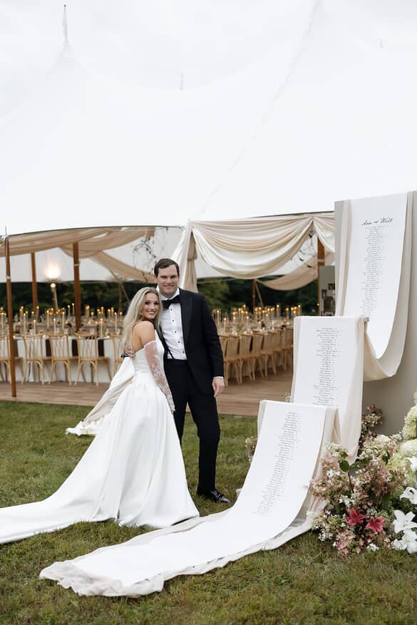happy newly married couple standing by their custom printed fabric wedding reception banner.